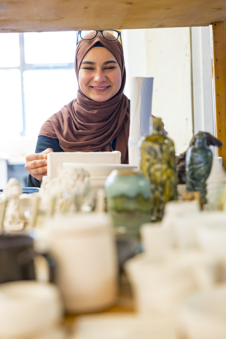 smiling art student with pottery and art equipment in the foreground