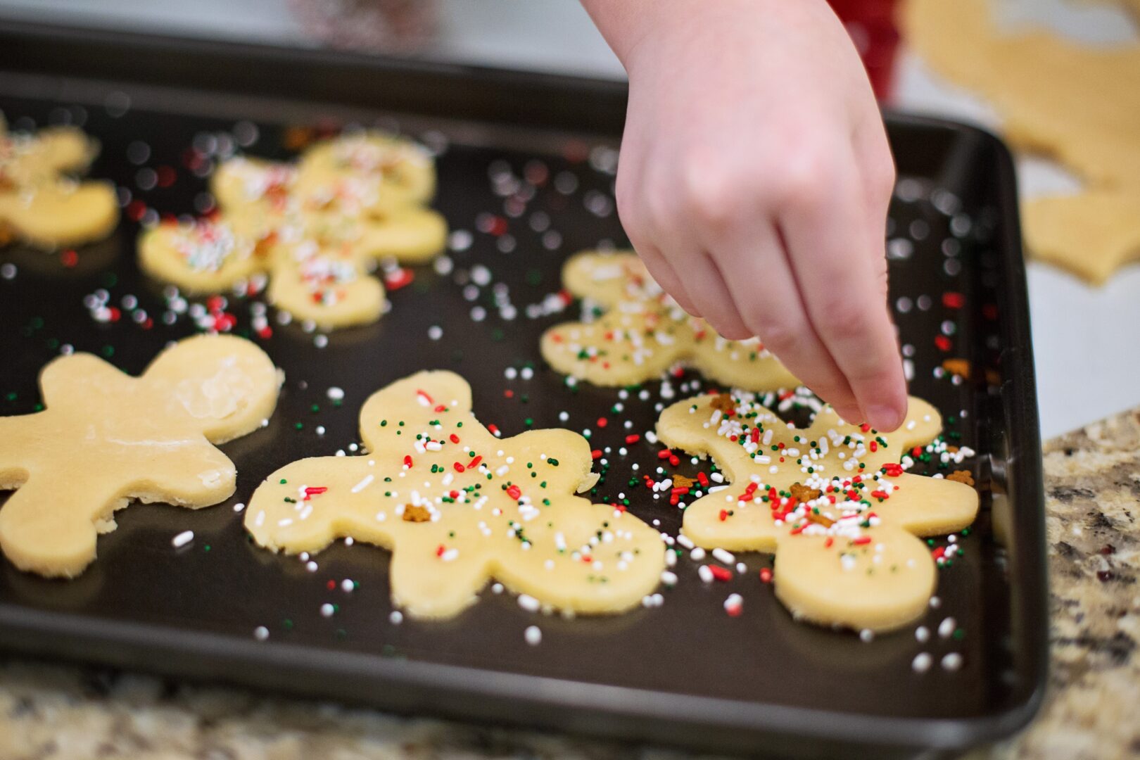 a hand placing sprinkles on gingerbread dough