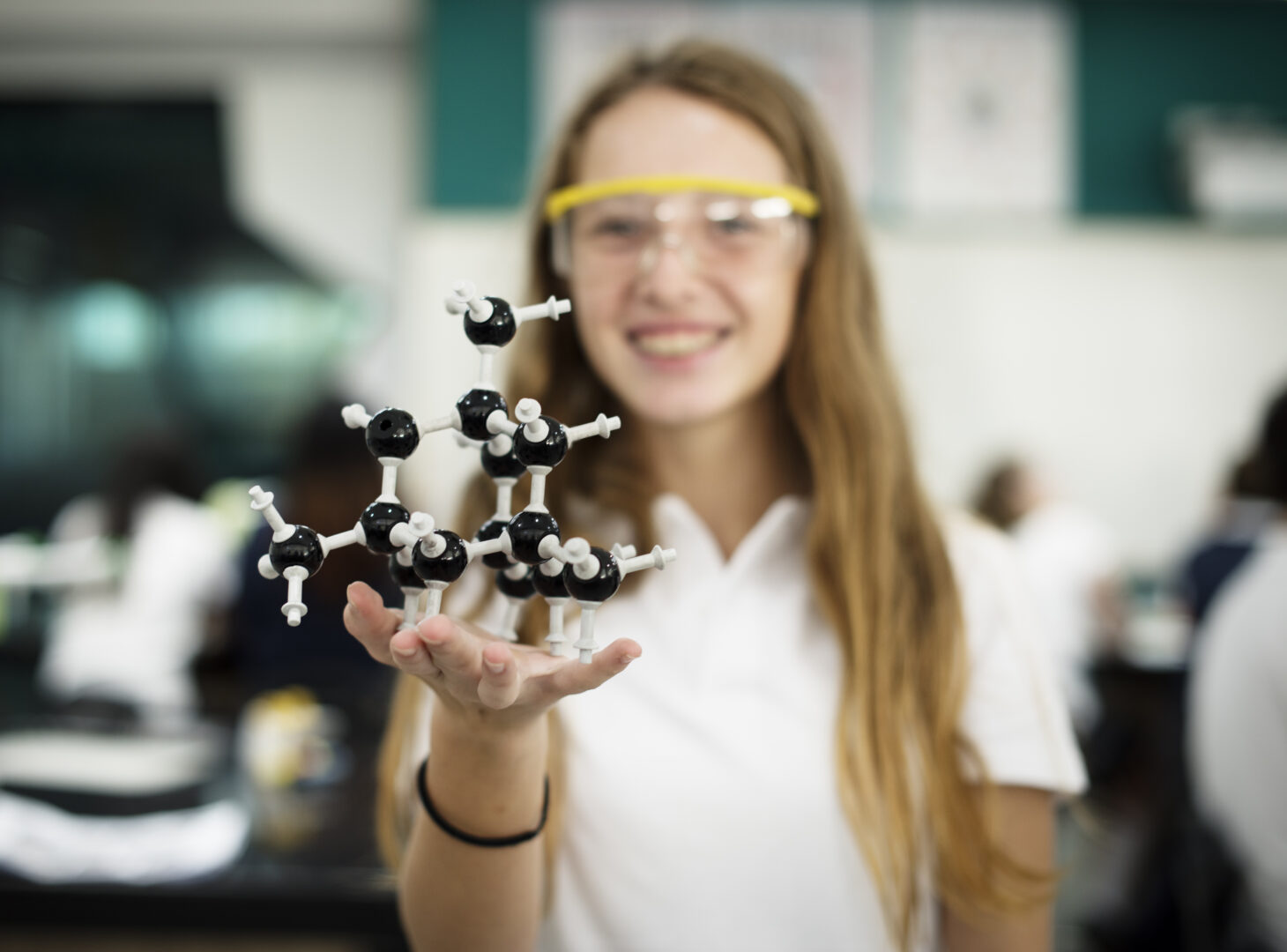 a young girl stands smiling wearing science safety goggles and she holds science equipment