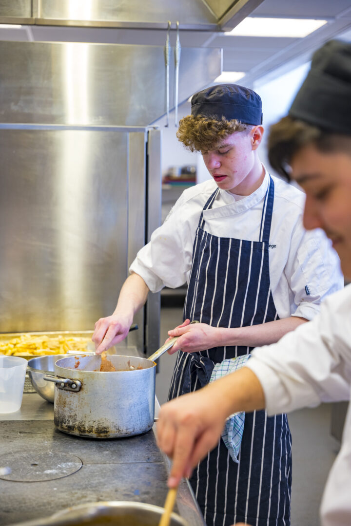 a catering student wearing an apron and hat cooking in the college kitchens