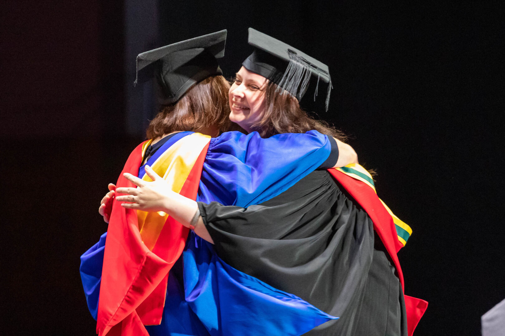 two hugging graduates on stage at their graduation