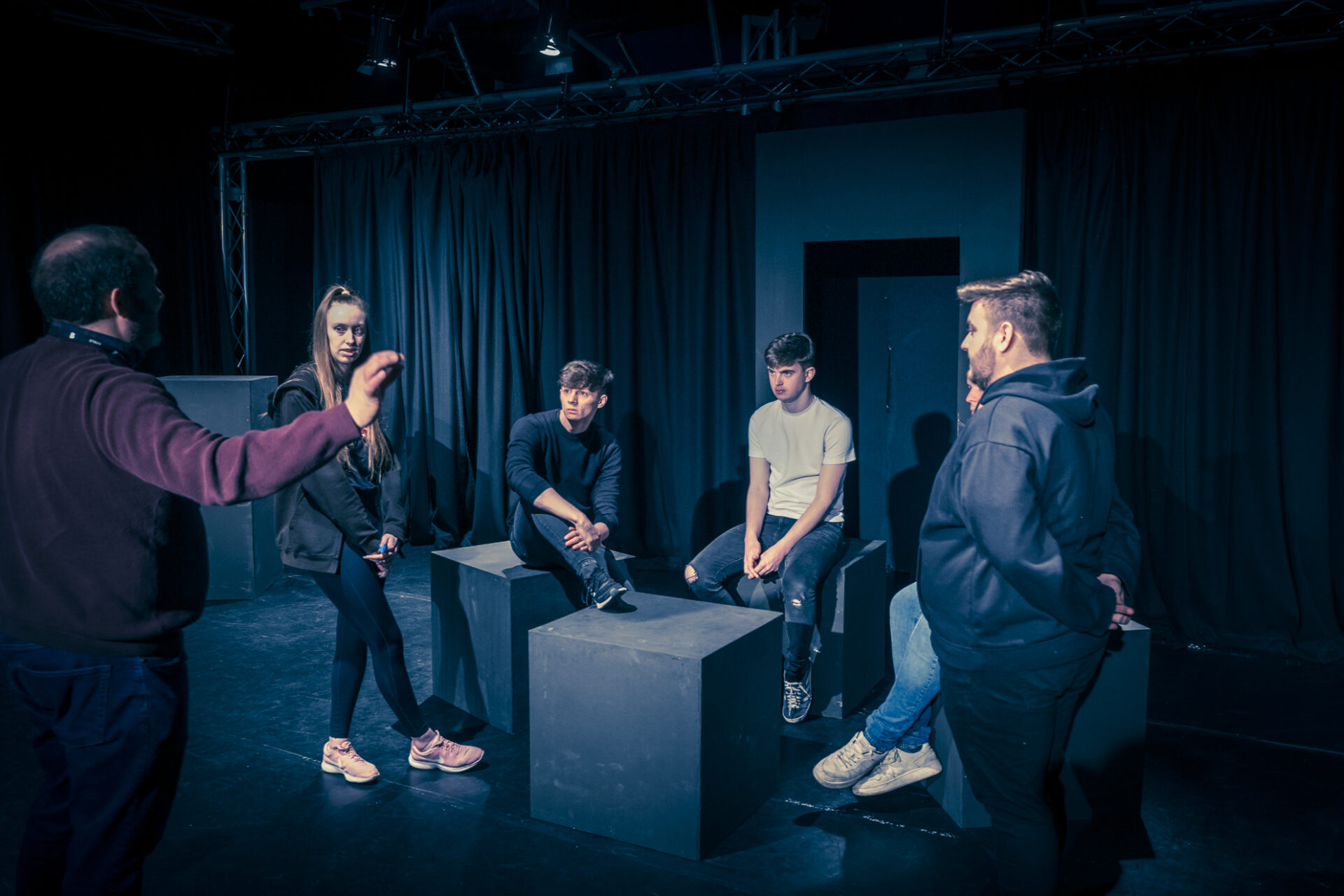 a group of performing arts student sit in a room as a teacher talks to them