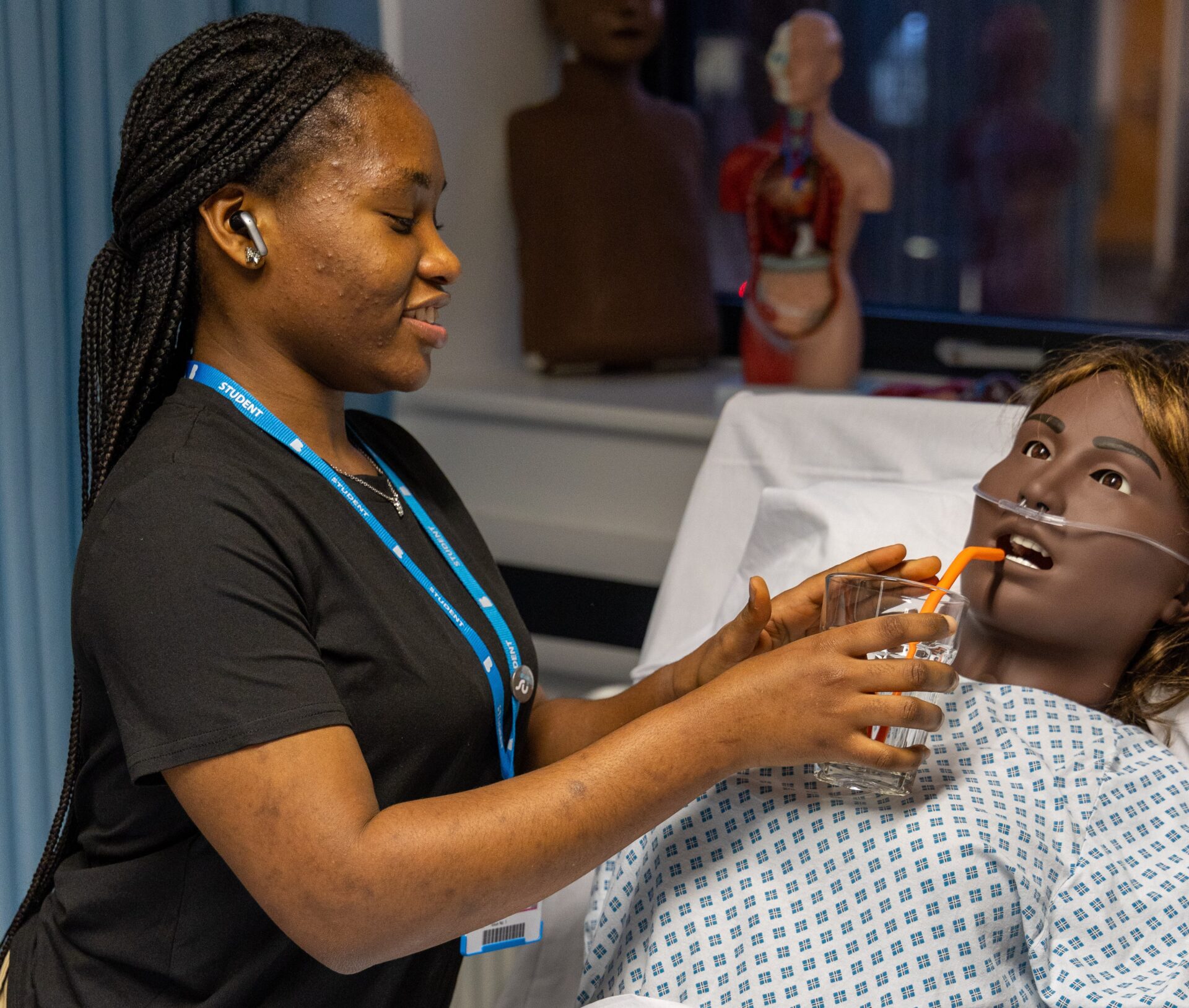 Female student giving a drink to training doll in our mock clinical ward