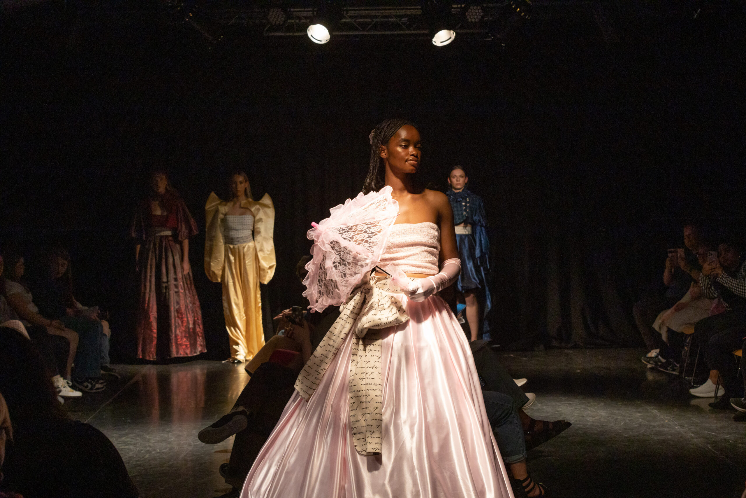 a model stands wearing a pink satin dress holding a lace covered umbrella