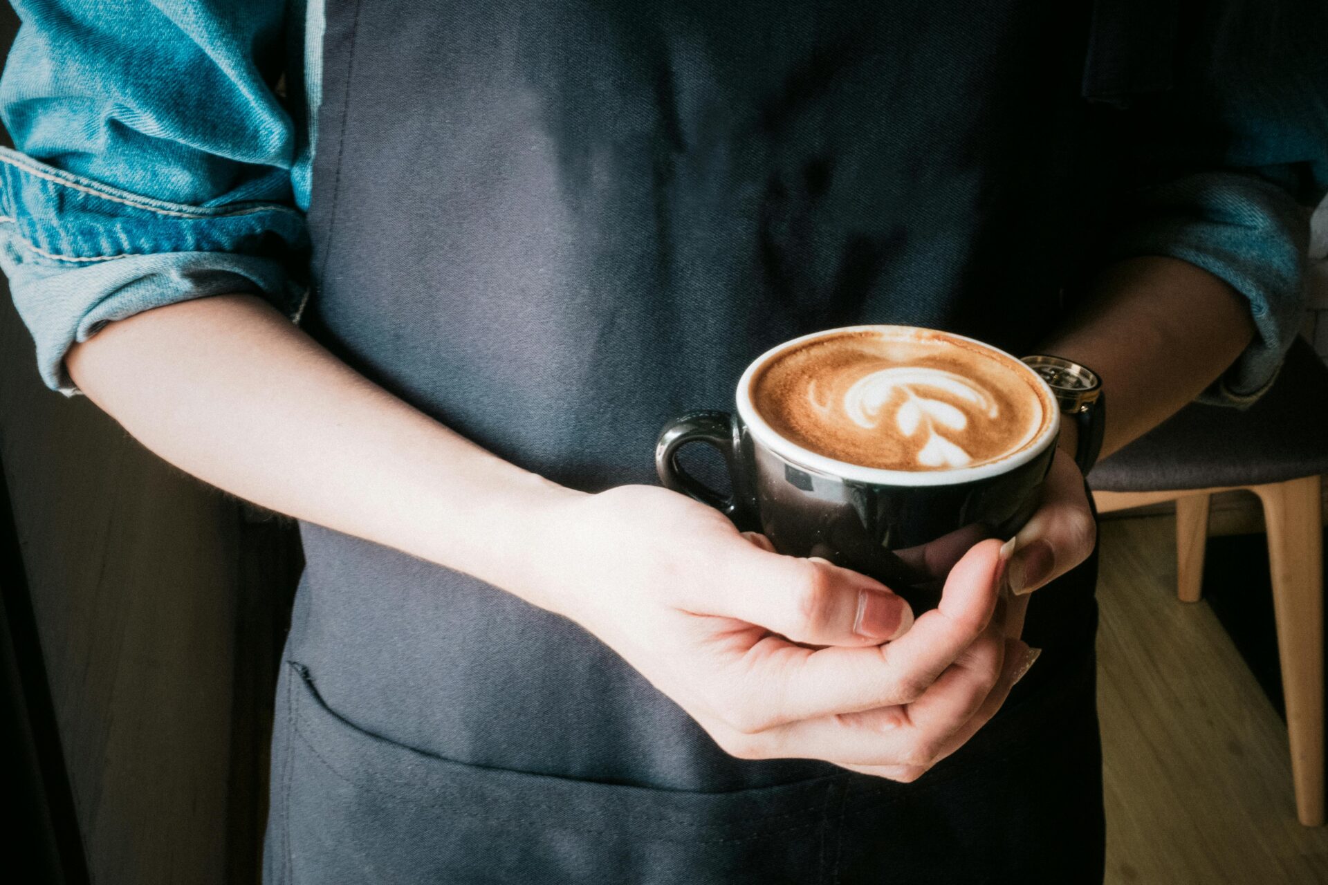 a barista stands holding a coffee as they wear an apron