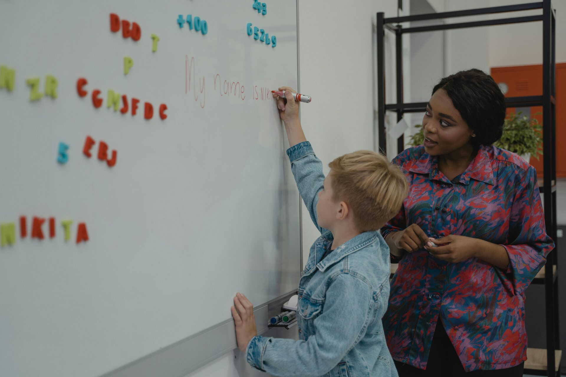 a teacher looks as a child writes on a whiteboard