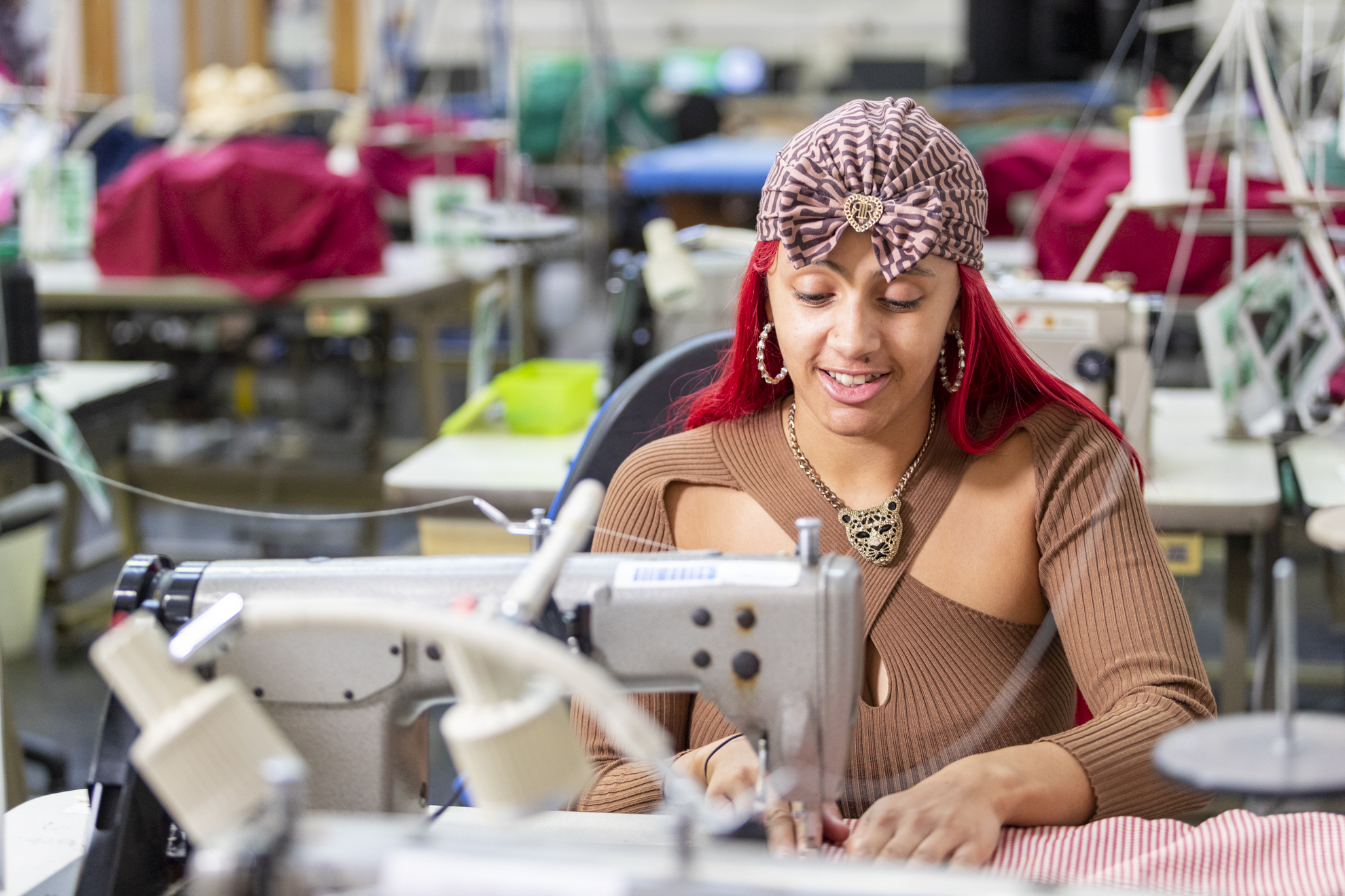 a fashion student sits smiling at a sewing machine