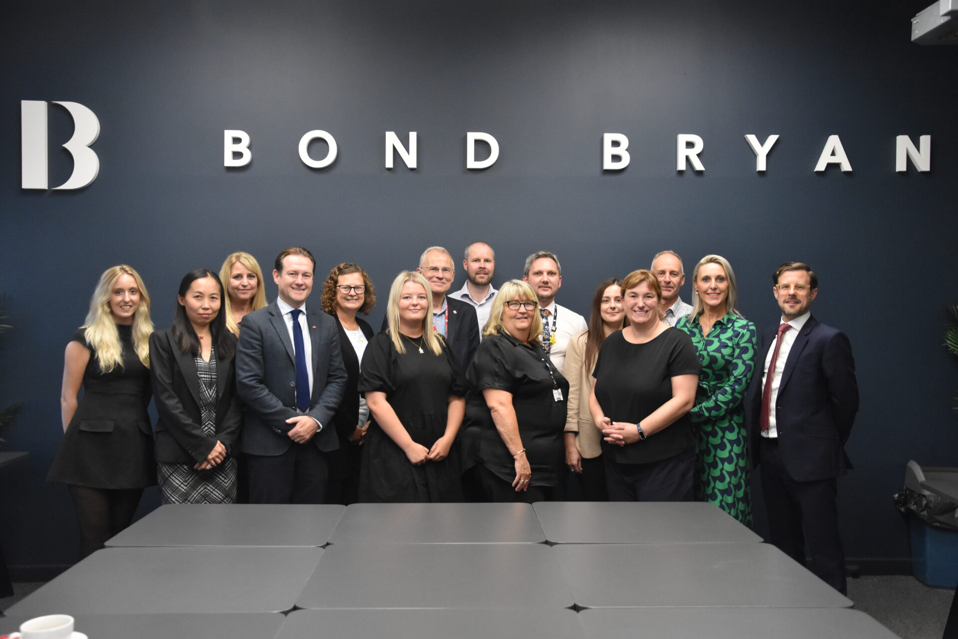 a group of people stand together in a room, some lettering on the wall behind them reads 'bond bryan'