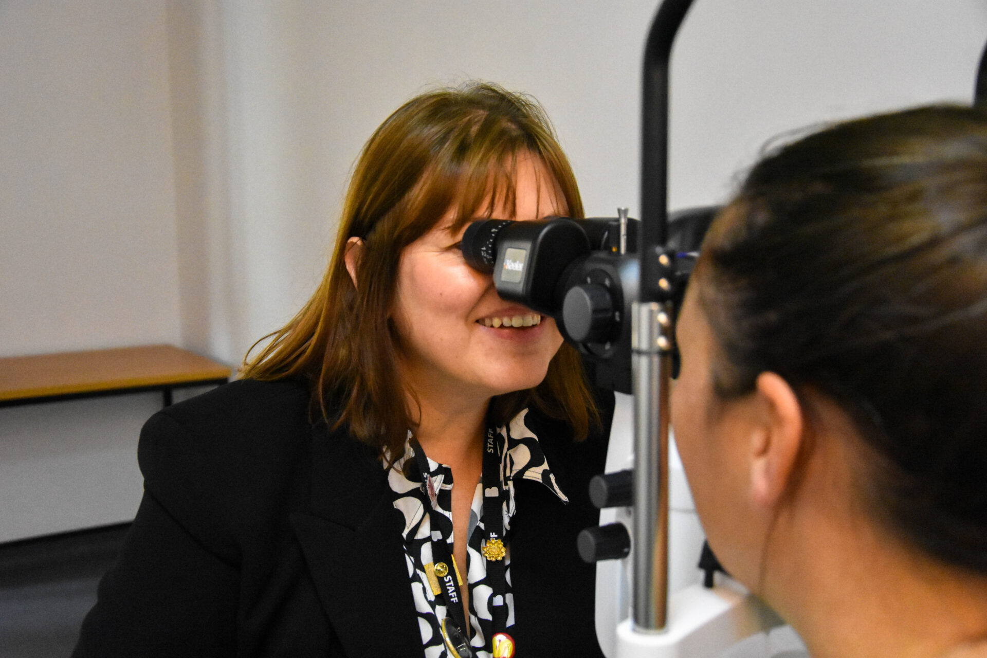 a dispensing optician looks through some equipment into the eyes of a patient in the foreground