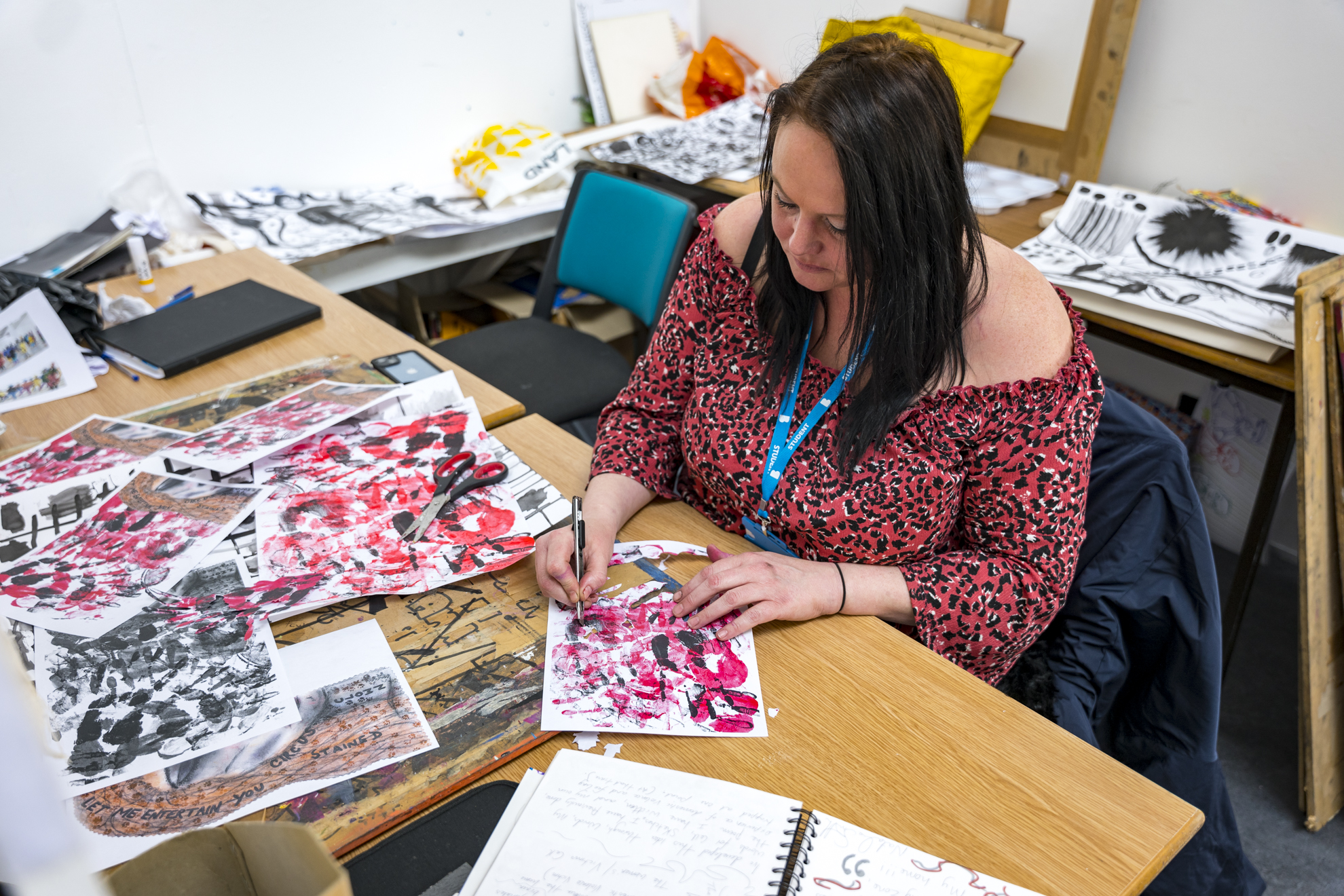 a student sits at a desk drawing black and pink illustrations on some paper