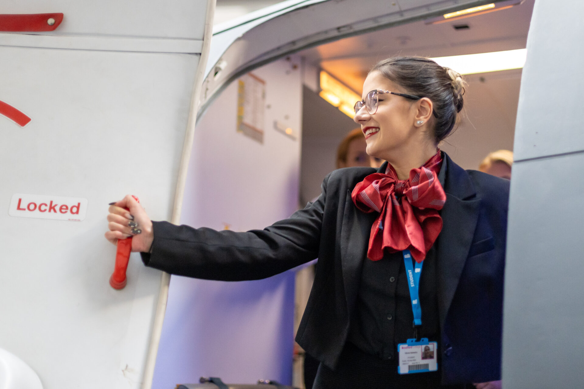 a smiling student wearing a flight attendant uniform smiles as she shuts the door of an aeroplane