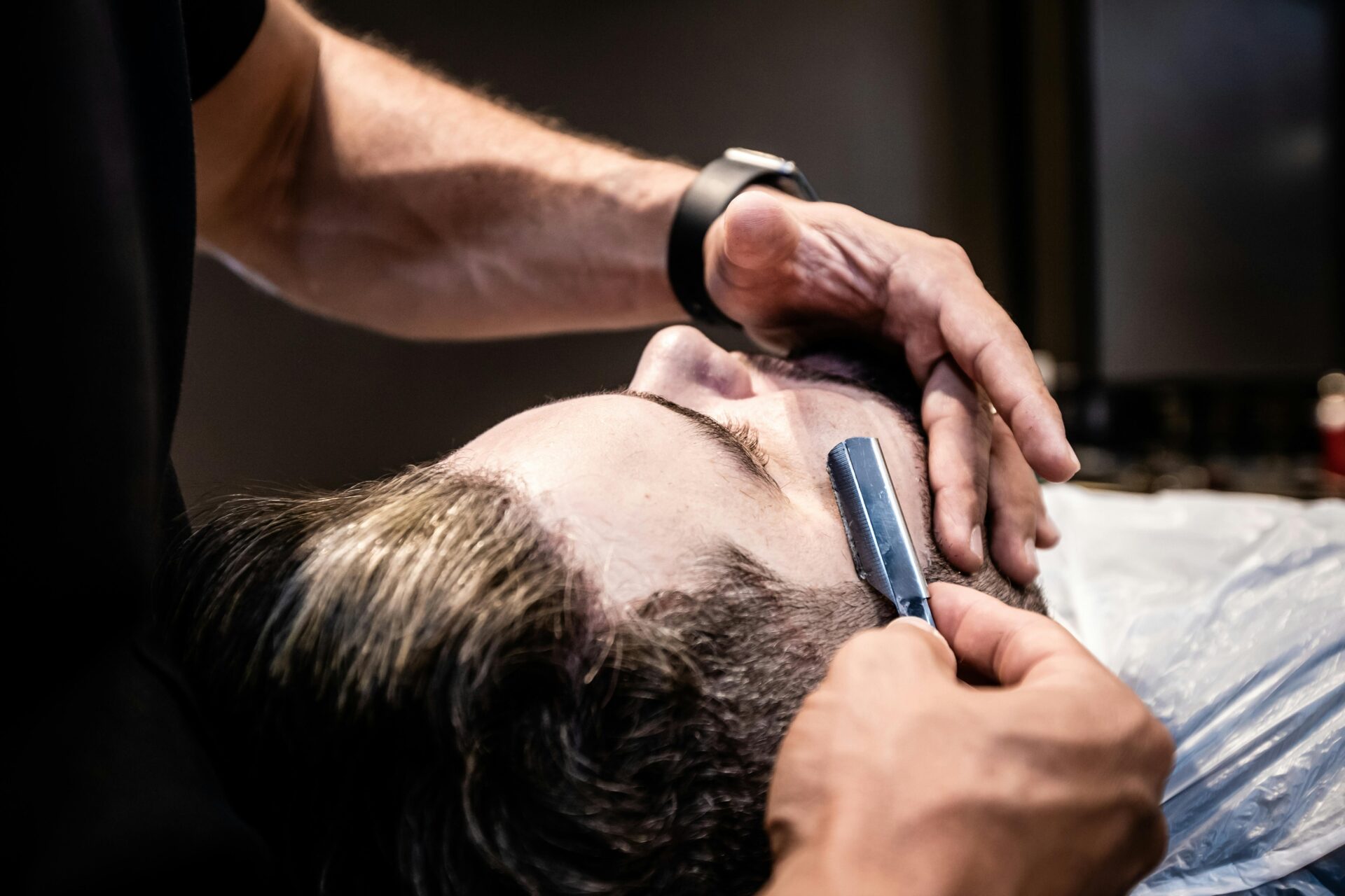 a customer sits back as a barber cuts his beard