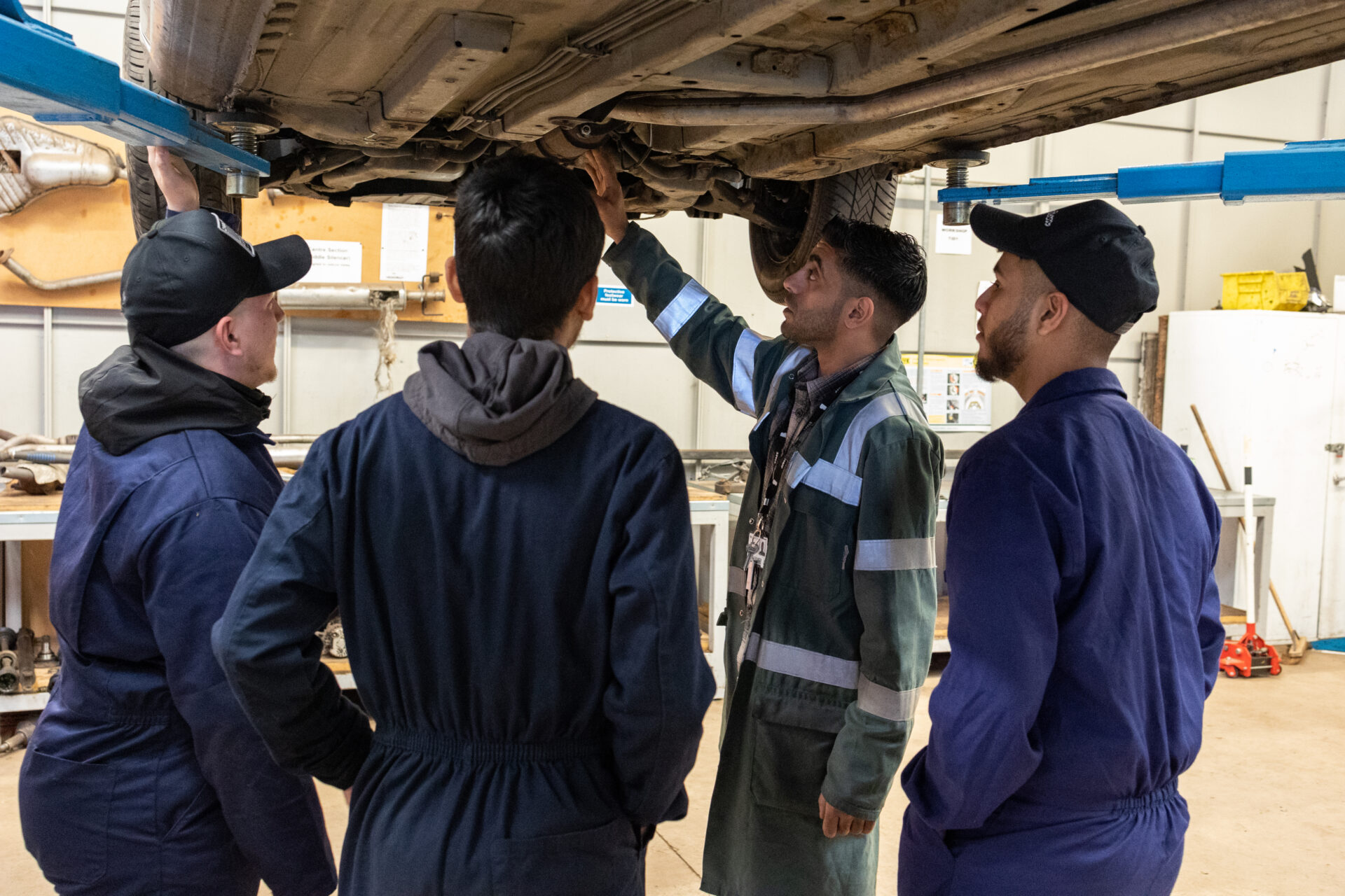 a group of automotive students stand together as a car is lifted above them