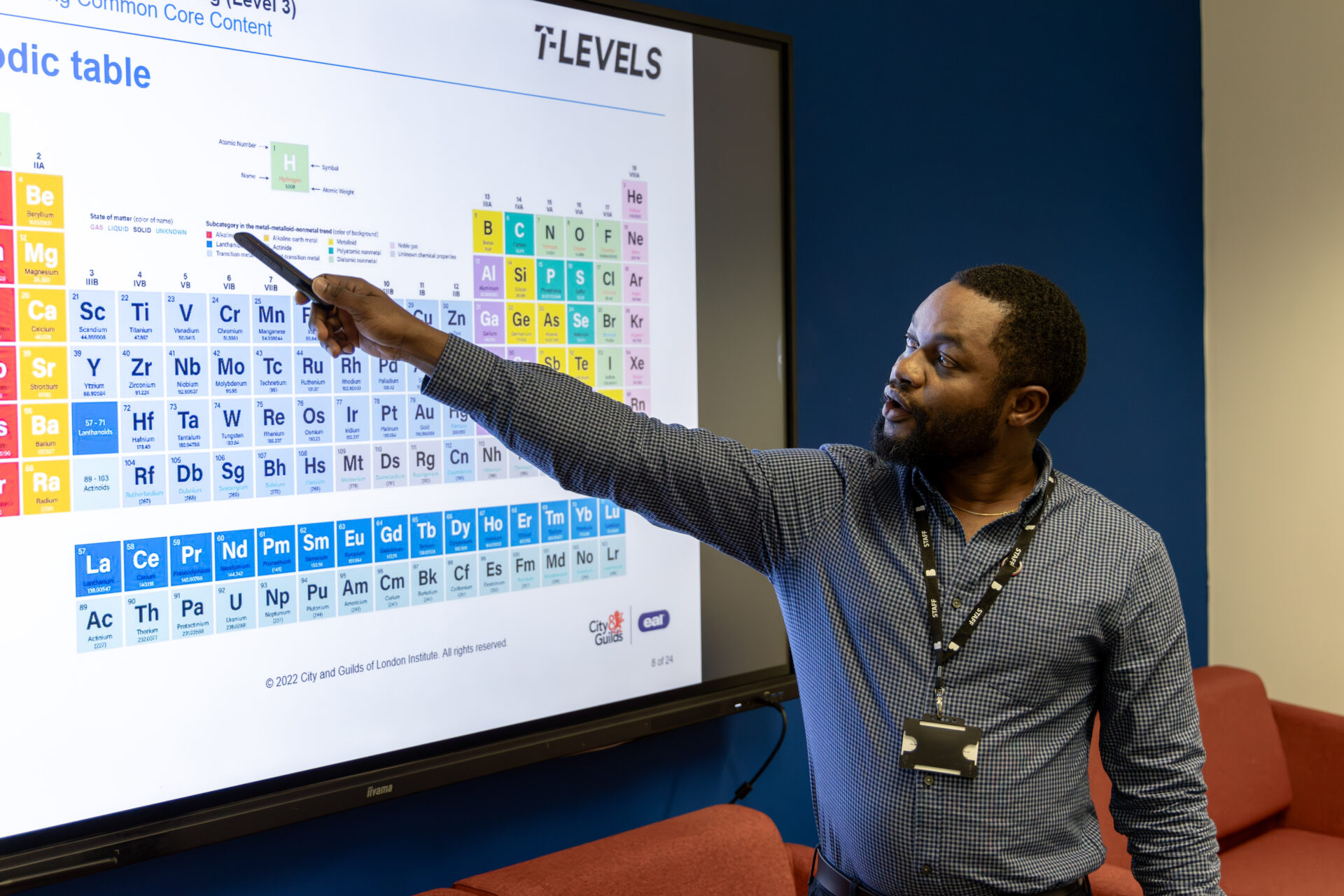 Male tutor point to whiteboard that has the periodic table on display