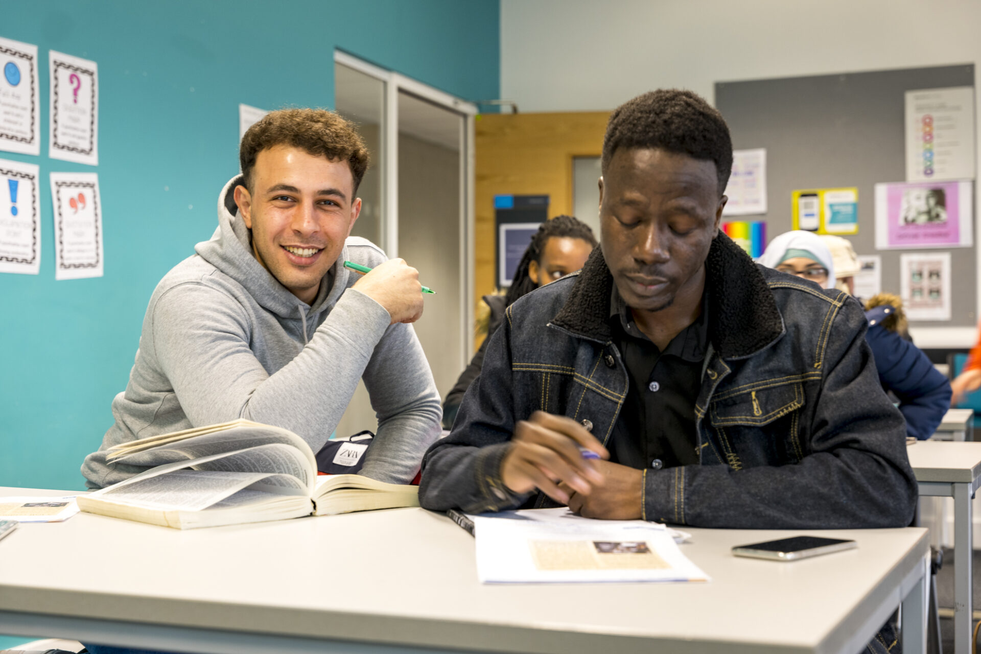 2 male students sat doing work at a desk in a class room